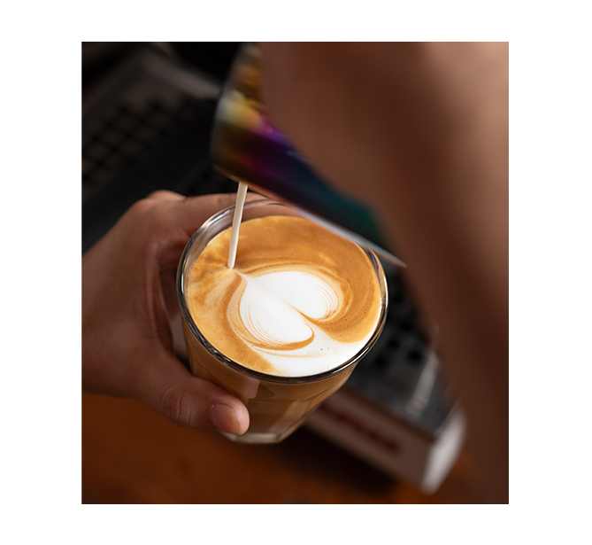 A barista pours steamed milk into espresso, creating a heart-shaped latte art pattern, showcasing the intricate craft of coffee making